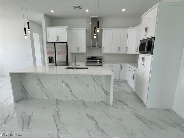 kitchen with a sink, wall chimney range hood, appliances with stainless steel finishes, white cabinetry, and a center island with sink