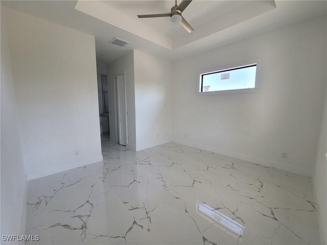 empty room with a raised ceiling, marble finish floor, a ceiling fan, and visible vents