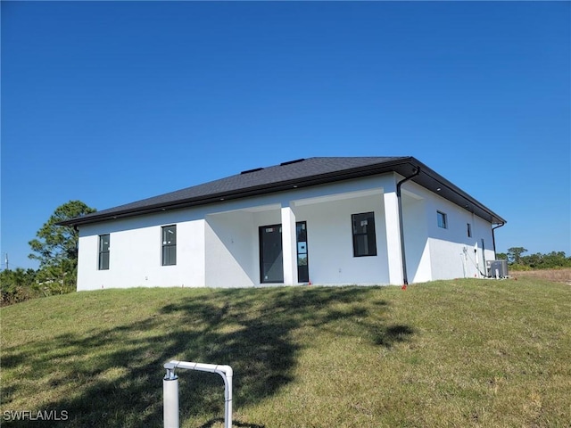back of property featuring central air condition unit, stucco siding, and a lawn