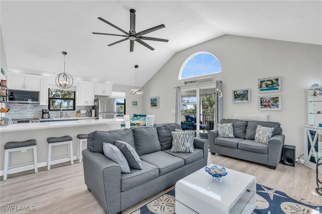 living room with ceiling fan with notable chandelier, high vaulted ceiling, and light wood-style floors