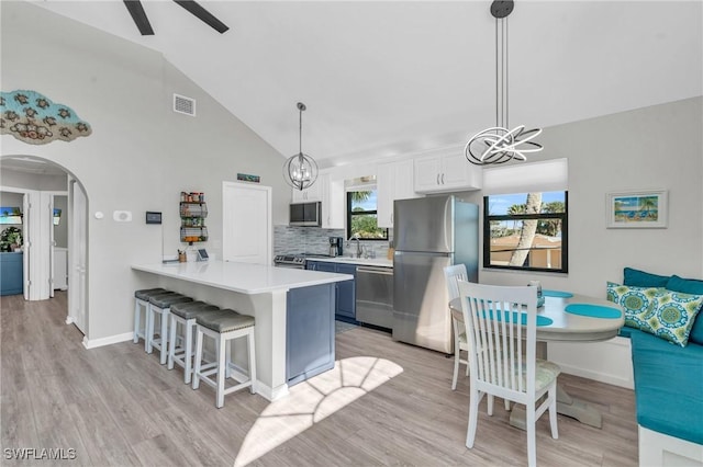 kitchen featuring light countertops, appliances with stainless steel finishes, white cabinetry, a peninsula, and a kitchen bar