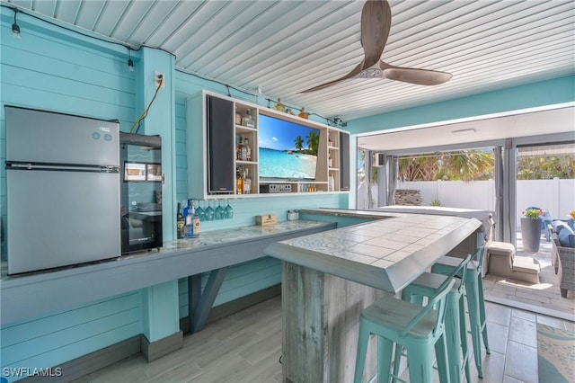 kitchen featuring light countertops, a breakfast bar area, freestanding refrigerator, and a ceiling fan