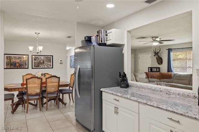 kitchen featuring stainless steel refrigerator, hanging light fixtures, light tile patterned floors, white cabinets, and ceiling fan with notable chandelier