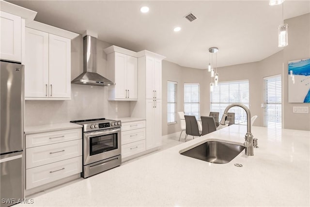 kitchen featuring white cabinets, stainless steel appliances, pendant lighting, wall chimney exhaust hood, and sink