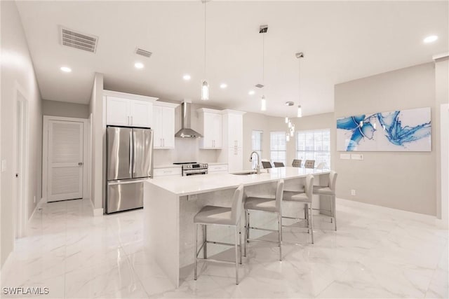 kitchen with stainless steel appliances, decorative light fixtures, white cabinets, a large island with sink, and wall chimney range hood