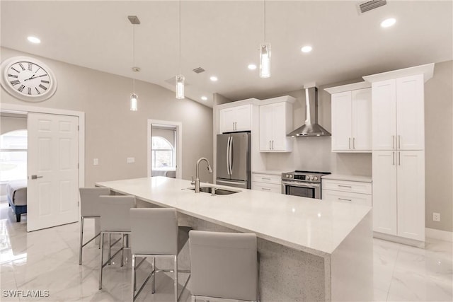 kitchen with stainless steel appliances, decorative light fixtures, wall chimney range hood, and a kitchen island with sink