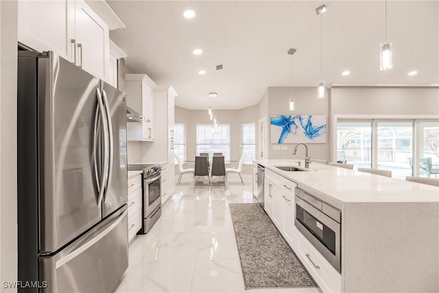 kitchen with stainless steel appliances, sink, white cabinetry, pendant lighting, and a kitchen island with sink