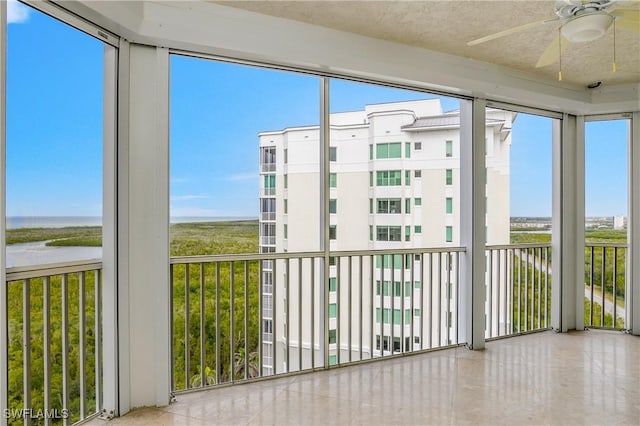 unfurnished sunroom featuring ceiling fan, a water view, and a healthy amount of sunlight