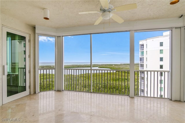 unfurnished sunroom featuring ceiling fan and a water view