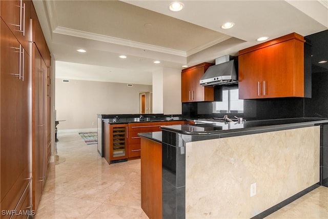 kitchen featuring wine cooler, wall chimney range hood, a raised ceiling, kitchen peninsula, and ornamental molding