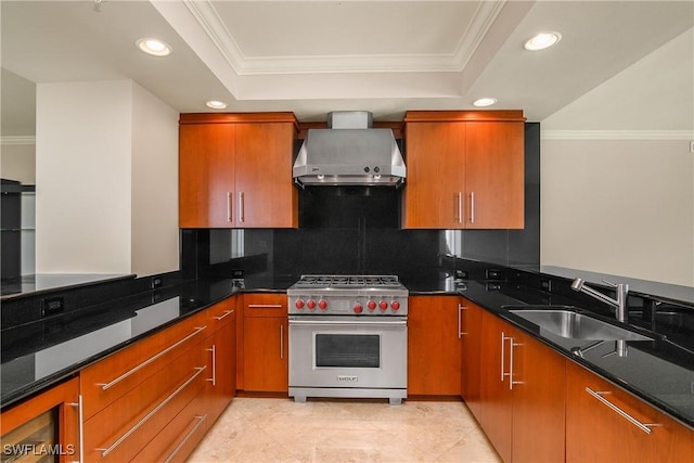 kitchen with wall chimney exhaust hood, dark stone countertops, designer range, a raised ceiling, and crown molding