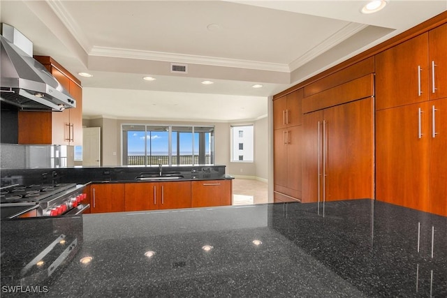 kitchen featuring paneled built in fridge, dark stone counters, wall chimney range hood, stainless steel range oven, and sink