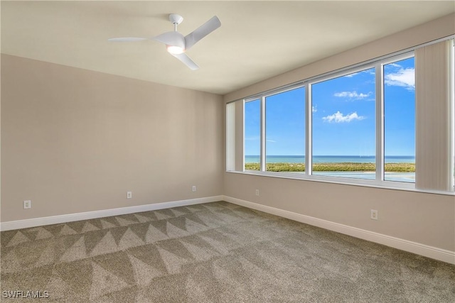 carpeted spare room featuring ceiling fan and a water view