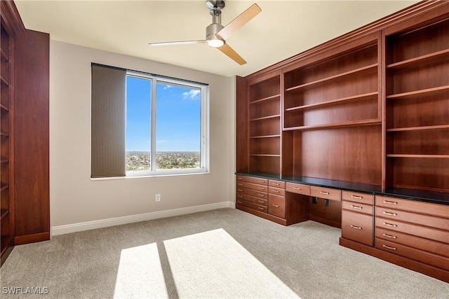 unfurnished office with light carpet, ceiling fan, and built in desk