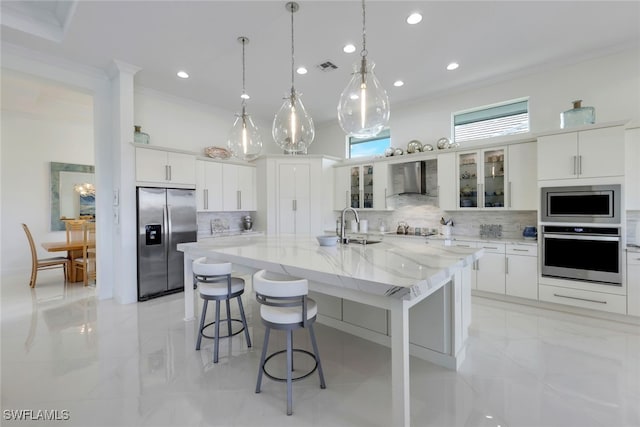 kitchen with stainless steel appliances, backsplash, a kitchen island with sink, wall chimney range hood, and white cabinets