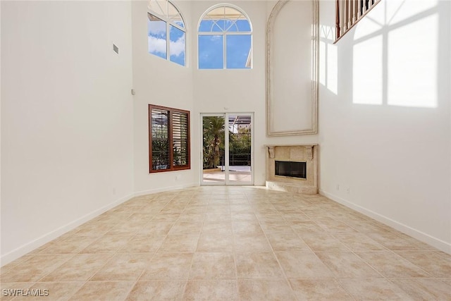 unfurnished living room featuring light tile patterned floors, a high end fireplace, and a towering ceiling