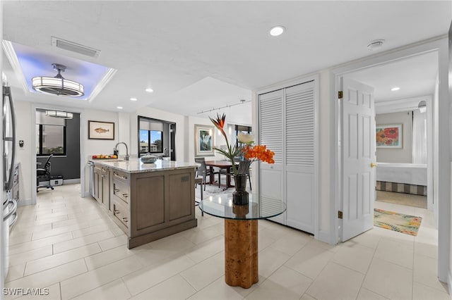 kitchen featuring sink, light tile patterned flooring, a kitchen island with sink, and light stone countertops