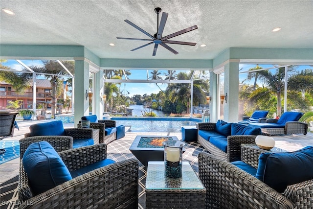 view of patio featuring a water view, ceiling fan, an outdoor living space with a fire pit, and glass enclosure