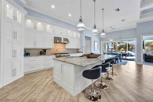 kitchen with white cabinetry, wall chimney exhaust hood, and a center island with sink