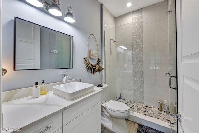 bathroom featuring toilet, vanity, wood-type flooring, and a shower with door