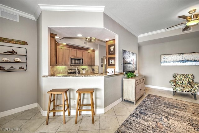 kitchen featuring a kitchen breakfast bar, ornamental molding, light tile patterned floors, kitchen peninsula, and stainless steel appliances