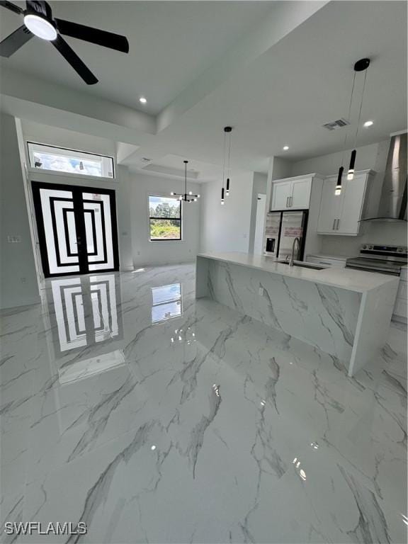 kitchen with hanging light fixtures, a center island with sink, wall chimney range hood, white cabinets, and sink