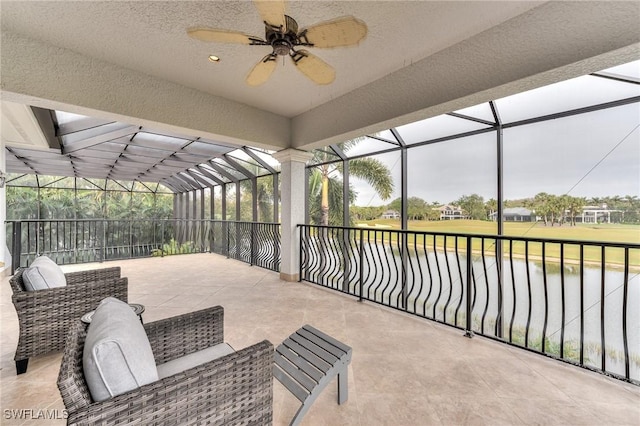 view of patio with ceiling fan, a water view, and glass enclosure