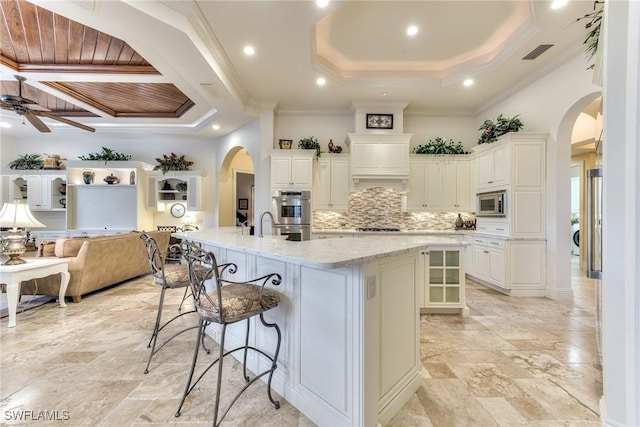 kitchen with a kitchen bar, a large island, ceiling fan, light stone countertops, and crown molding