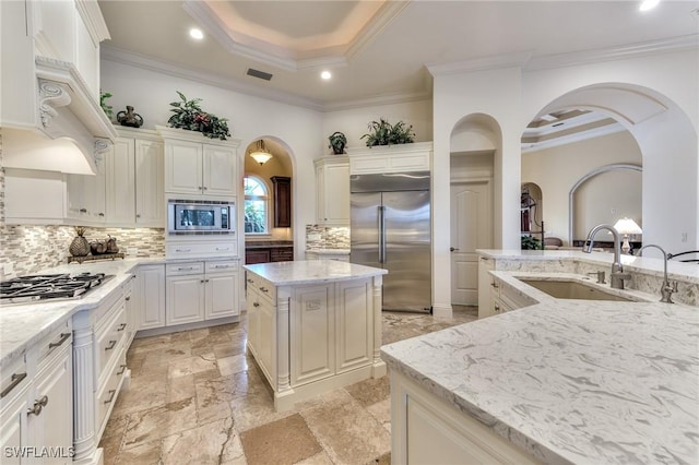 kitchen featuring a raised ceiling, backsplash, light stone countertops, built in appliances, and a center island