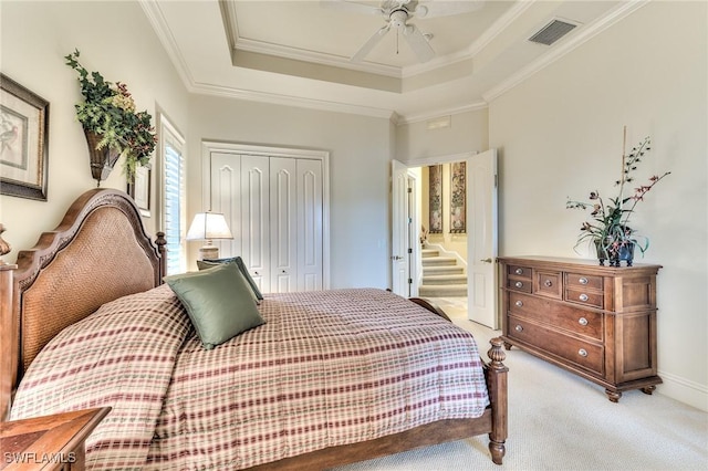 bedroom featuring ceiling fan, a raised ceiling, a closet, light colored carpet, and ornamental molding