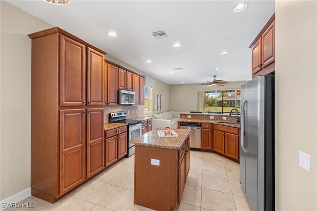 kitchen with light tile patterned floors, ceiling fan, appliances with stainless steel finishes, a kitchen island, and sink