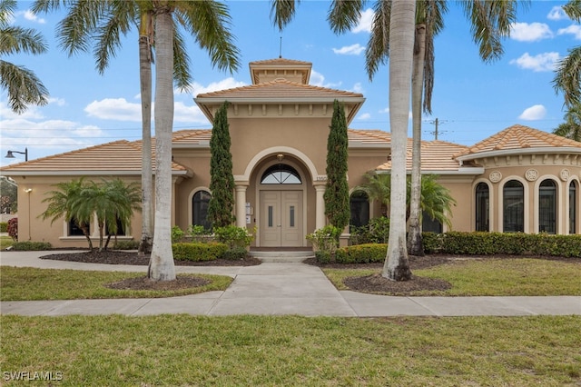 mediterranean / spanish house with a tiled roof, a front yard, and stucco siding