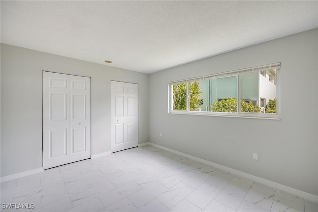 unfurnished bedroom featuring a textured ceiling and two closets