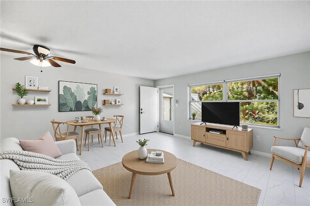 living area featuring baseboards, marble finish floor, and ceiling fan