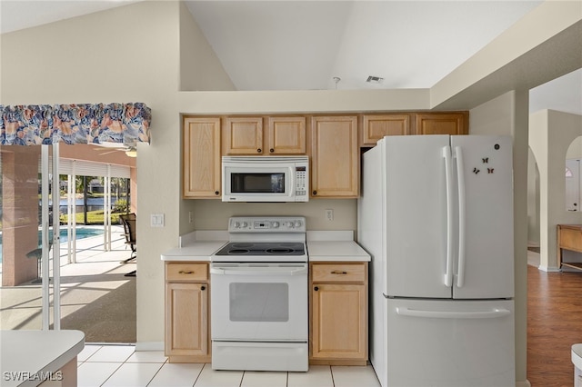 kitchen featuring white appliances, light tile patterned flooring, lofted ceiling, and light brown cabinets