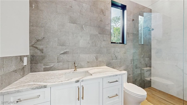 bathroom featuring tile walls, a tile shower, hardwood / wood-style floors, toilet, and vanity