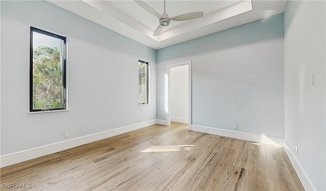 unfurnished room featuring light wood-type flooring, ceiling fan, a wealth of natural light, and a tray ceiling