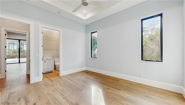 unfurnished bedroom with ceiling fan, multiple windows, a tray ceiling, and ensuite bath