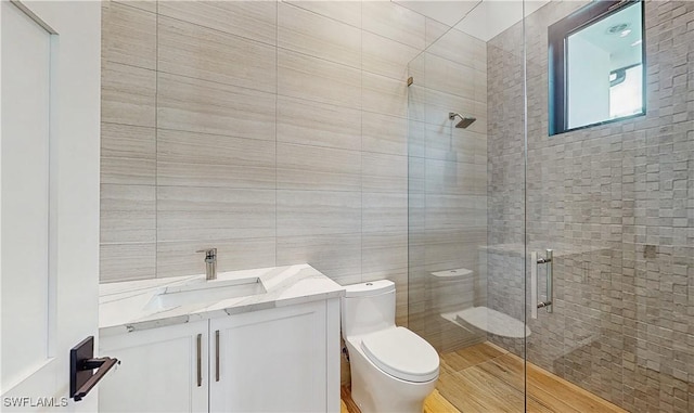 bathroom featuring a shower with door, toilet, vanity, and tile walls