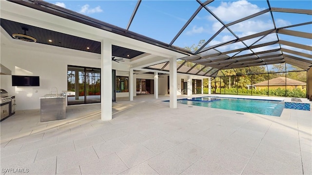 view of swimming pool with glass enclosure, exterior kitchen, a patio, ceiling fan, and pool water feature