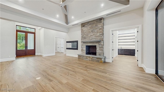 unfurnished living room featuring a fireplace, light wood-type flooring, a high ceiling, and french doors