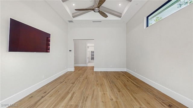 unfurnished room featuring a towering ceiling, light hardwood / wood-style flooring, beamed ceiling, and ceiling fan