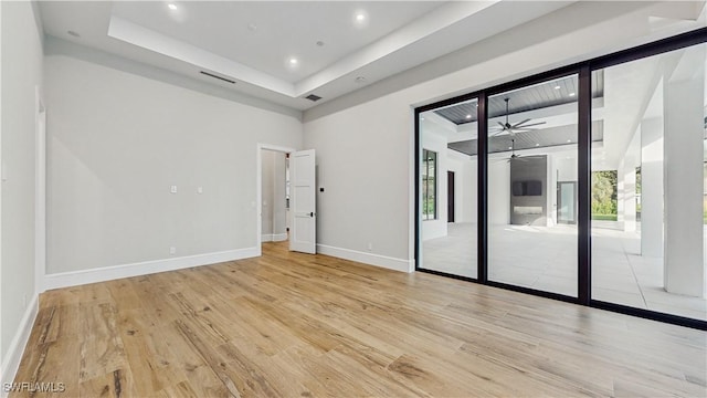 unfurnished room with ceiling fan, a raised ceiling, and light hardwood / wood-style floors