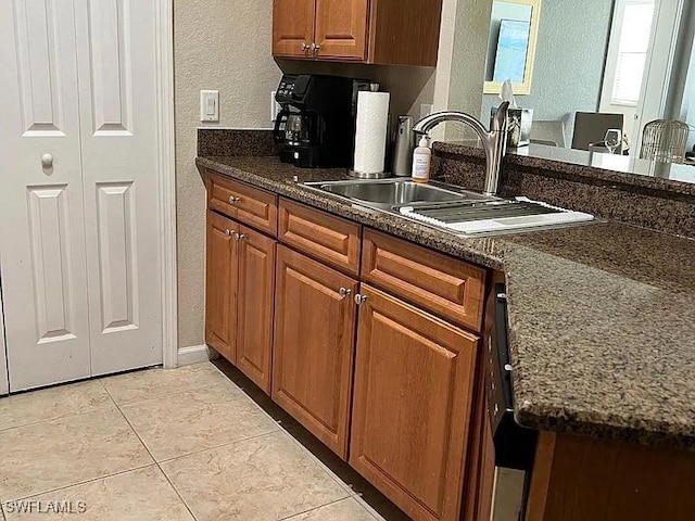 kitchen with light tile patterned floors, dark stone countertops, and sink