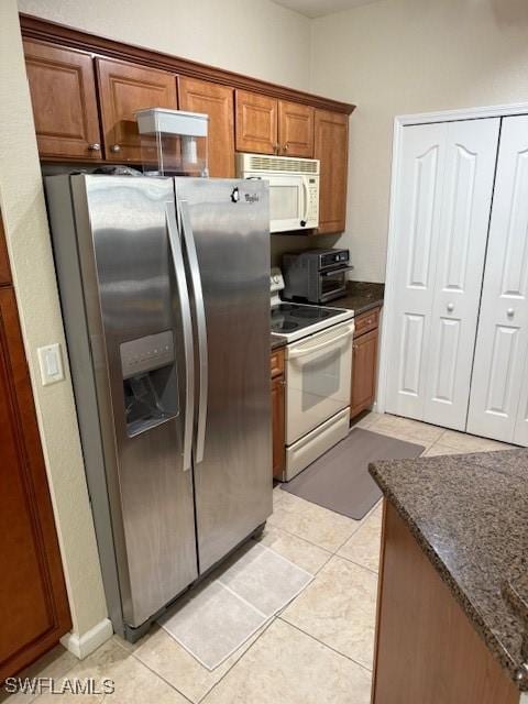 kitchen with light tile patterned floors, white appliances, and dark stone counters