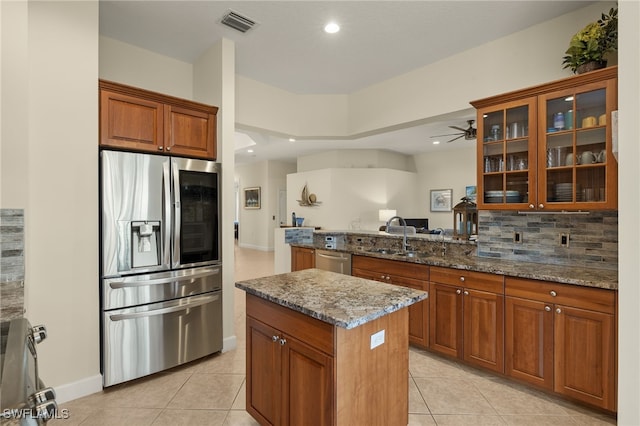 kitchen featuring stainless steel appliances, sink, a center island, kitchen peninsula, and stone countertops