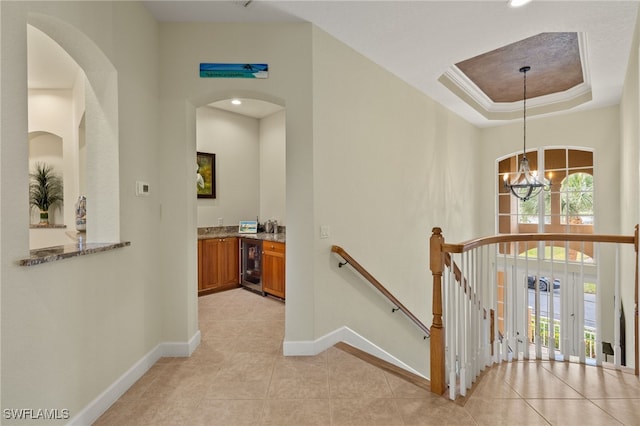 hallway featuring a healthy amount of sunlight, beverage cooler, a raised ceiling, and a chandelier