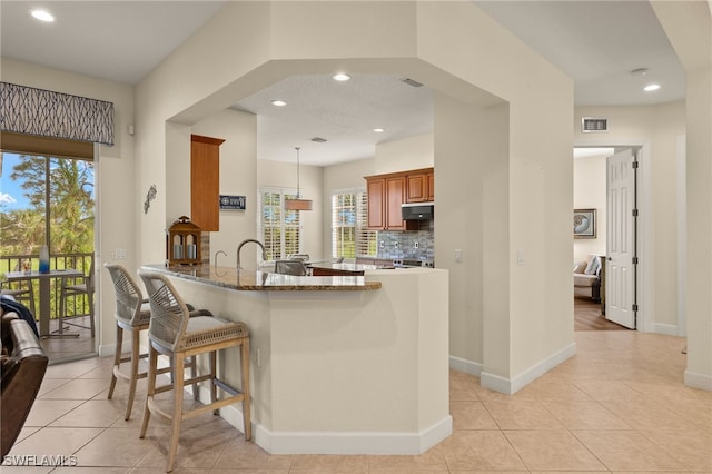 kitchen featuring kitchen peninsula, light tile patterned flooring, a kitchen breakfast bar, and light stone countertops