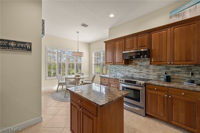 kitchen featuring stainless steel appliances, a center island, light tile patterned floors, dark stone counters, and hanging light fixtures