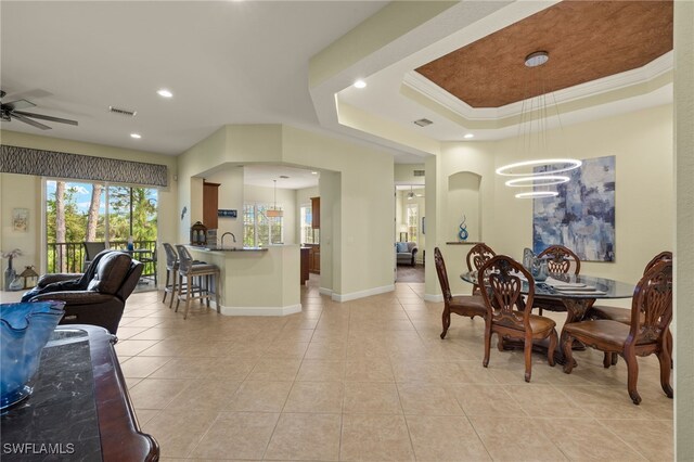 dining room with ornamental molding, light tile patterned floors, ceiling fan with notable chandelier, and a tray ceiling